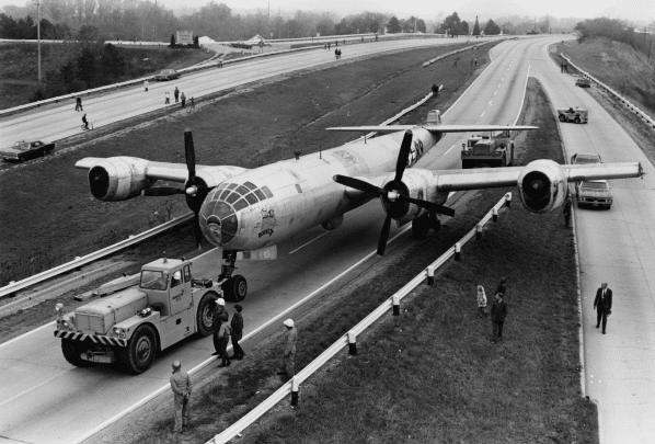 People, vehicles, and an aircraft in black and white.