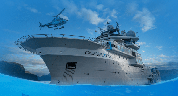OceanXplorer ship against a blue sky and blue sea with a helicopter above.